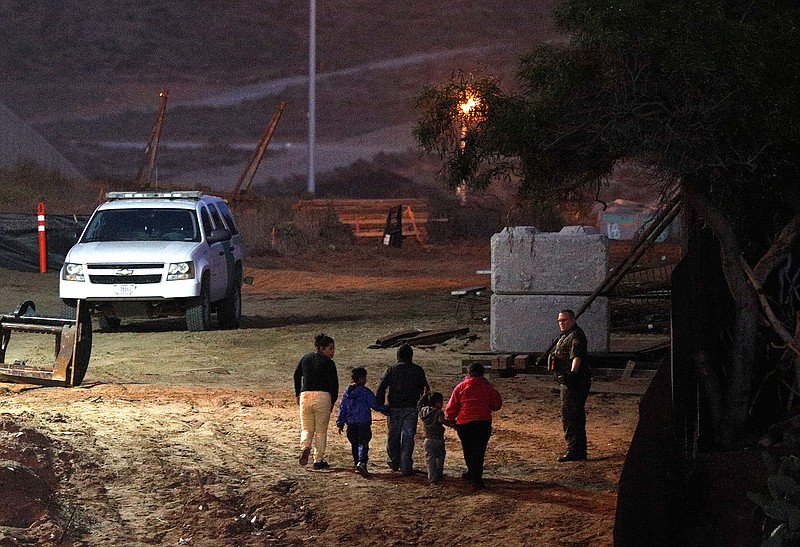 Migrants traveling with children walk up a hill to a waiting U.S. Border Patrol agent just inside San Ysidro, Calif., after climbing over the border wall from Playas de Tijuana, Mexico, Monday, Dec. 3, 2018. Thousands of Central American migrants who traveled with recent caravans want to seek asylum in the United States but face a decision between crossing illegally or waiting months, because the U.S. government only processes a limited number of those cases a day at the San Ysidro border crossing. (AP Photo/Rebecca Blackwell)