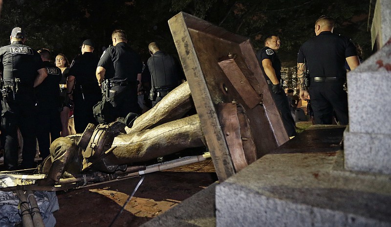 FILE - In this Monday, Aug. 20, 2018, file photo, police stand guard after the Confederate statue known as Silent Sam was toppled by protesters on campus at the University of North Carolina in Chapel Hill, N.C. The board overseeing North Carolina’s public universities is meeting to decide the fate of "Silent Sam."  The University of North Carolina System Board of Governors was meeting Friday, Dec. 14, to discuss a proposal to build a $5 million building to house the statue at UNC-Chapel Hill.  (AP Photo/Gerry Broome, File)