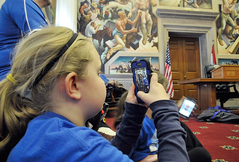 In this March 5, 2015 photo, Dacey Colbert uses her phone to take photos of the Thomas Hart Benton mural in the House of Representatives Lounge as Russellville Elementary School fourth graders visited the Missouri State Capitol.