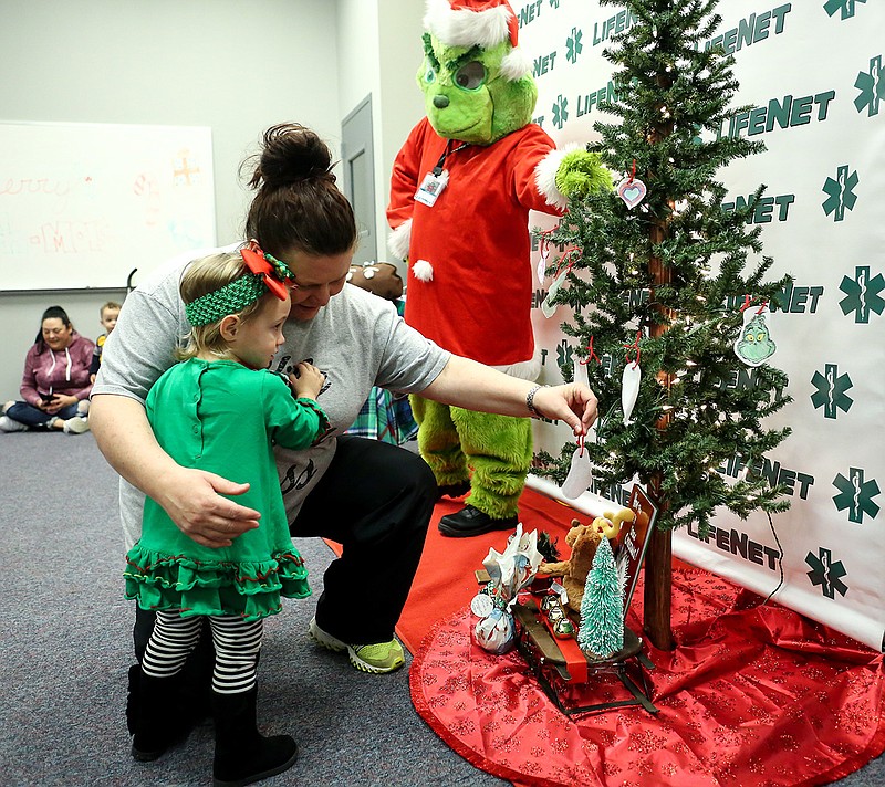 Jackie Trusty hangs a paper ornament that her daughter, Isabella, made on the Christmas tree on Monday in Texarkana, Texas at LifeNet's Christmas Photos with the Grinch event. Children could have their pictures made with the Grinch and participate in craft activities.