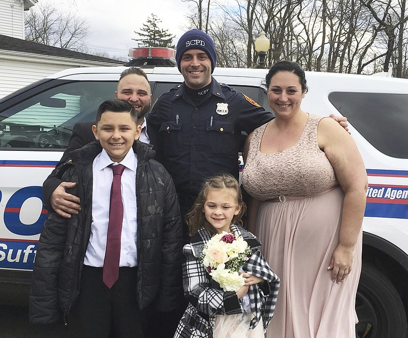 In this photo provided by the Suffolk County Police Department, Suffolk County Police Officer Cody Matthews, center, poses with a family after driving them to Town Hall in the Village of Lake Grove, N.Y., where the couple got married, Saturday, Dec. 22, 2018. They were on the way to the couple's wedding when their vehicle was involved in an accident. Matthews drove them to their wedding in his police vehicle and served as an official witness. In the back from left are Joseph DeMichele and Officer Cody Matthews. In the front row from left are Jayden Corriche, 10; Gianna DeMichele, 5, and Feliece Terwilliger. (Suffolk County Police Department via AP)