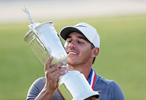 In this June 17, 2018, file photo, Brooks Koepka holds up the Golf Champion Trophy after winning the U.S. Open in Southampton, N.Y.  Koepka says the key to victory were 9-irons he hit on the 16th and 17th holes of the final round.