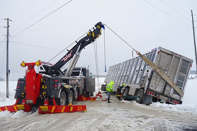 Tow vehicles work to maneuver a tractor trailer full of pigs back onto County Road 230. Slippery conditions complicated the operation, but the road was clear within about 90 minutes of the accident. 