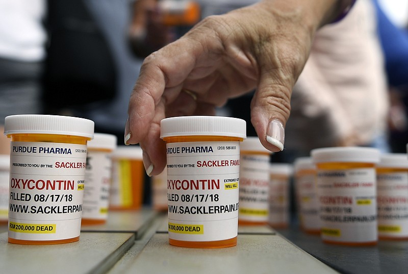 FILE - In this Aug. 17, 2018, file photo, family and friends who have lost loved ones to OxyContin and opioid overdoses leave pill bottles in protest outside the headquarters of Purdue Pharma, which is owned by the Sackler family, in Stamford, Conn. A new filing in a Massachusetts case ramps up the legal and financial pressure against the Sackler family, which owns the company that makes OxyContin.  (AP Photo/Jessica Hill, File)