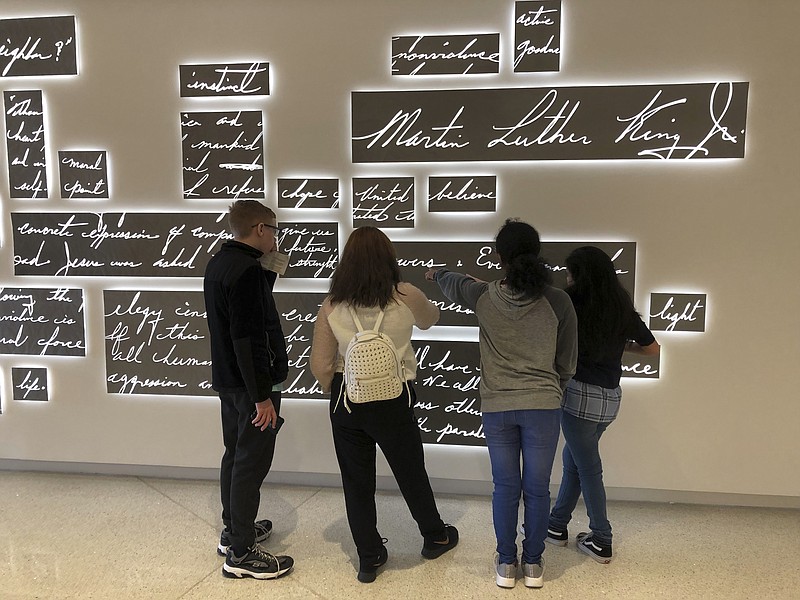 In this Friday, Jan. 18, 2019 photo, visitors look at a new metal sculpture at the National Center for Civil and Human Rights in Atlanta that features the words of the Rev. Martin Luther King Jr. in his own handwriting illuminated by light. The permanent sculpture hangs just outside a gallery where an exhibit of King's papers, including drafts of famous speeches and notable sermons, is on display. (AP Photo/Kate Brumback)