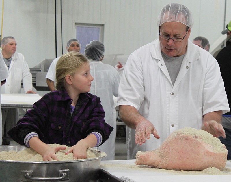 <p>Democrat photo/Liz Morales</p><p>Emma Gardner receives a lesson from Jeff Rayl on how to rub and spread cure onto a ham carcass Jan. 18, as part of a learning demonstration for 4-H members at Burgers’ Smokehouse.</p>