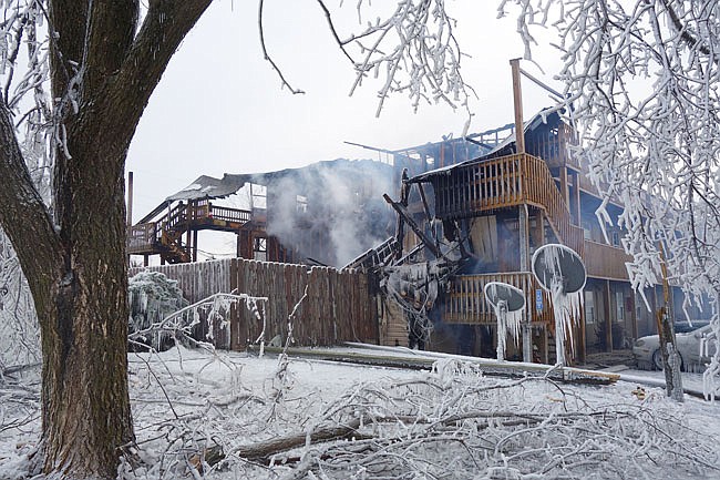 Ice coats trees and vehicles around Evergreen Apartments, while small fires still smolder in the complex's interior.          