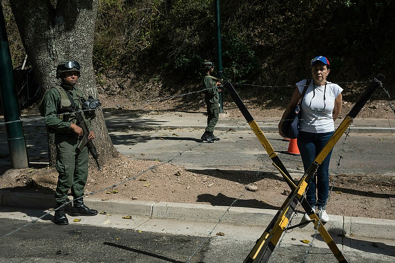 A woman stands next to soldiers as other members of the opposition hand out copies of an amnesty law near Ft. Tiuna military base in Caracas, Venezuela, Sunday, Jan. 27, 2019. Opposition National Assembly leader Juan Guaido, who declared himself interim president, said Friday that he would release the text of an existing amnesty law that would pardon members of the military who cooperate in restoring democracy and asked Venezuelans to share it with officers they know. (AP Photo/Rodrigo Abd)