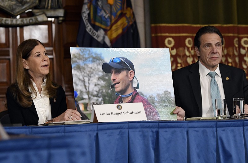 FILE - In this Tuesday, Jan. 29, 2019, file photo, Linda Beigel Schulman, left, holds a photograph of her son Scott Beigel, who was killed during the Valentine’s Day massacre at Marjory Stoneman Douglas High School, while speaking with New York Gov. Andrew Cuomo and gun safety advocates during a news conference at the state Capitol in Albany, N.Y. Since the shooting, states have seen a surge of interest in laws intended to make it easier to disarm people who show signs of being violent or suicidal. (AP Photo/Hans Pennink, File)