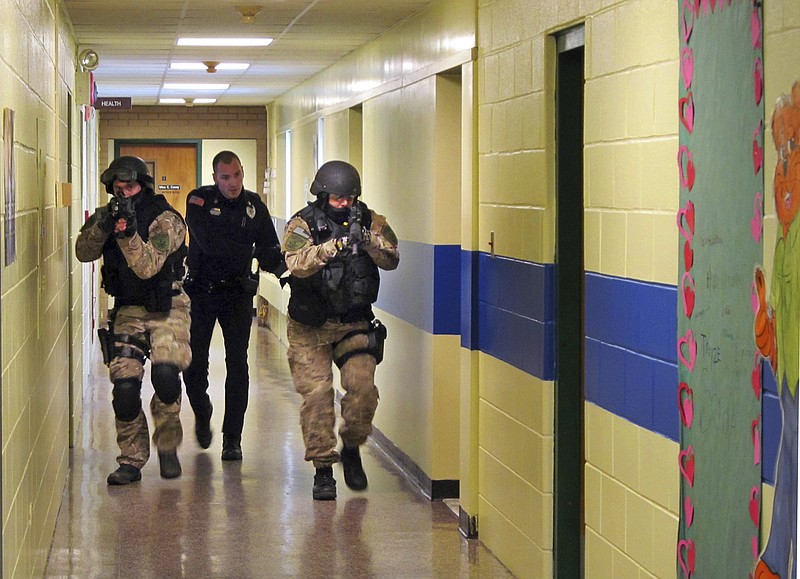 FILE - In this Jan. 28, 2013, file photo, members of the Washington County Sheriff's Office and the Hudson Falls Police Department use unloaded guns to take part in an emergency drill as they walk through a corridor inside the Hudson Falls Primary School in Hudson Falls, N.Y. With each subsequent shooting forcing schools to review their readiness, parents are increasingly questioning elements of the ever-evolving drills that are now part of most emergency plans, including the use of simulated gunfire and blood, when to reveal it’s just practice, and whether drills unduly traumatize kids. (Omar Ricardo Aquije/The Post-Star via AP, File)