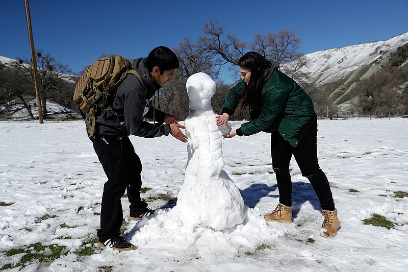 Michael Monsivais, left, makes a snowman Monday with the help of his girlfriend Torrie Martinez at Fort Tejon State Historic Park in Lebec, Calif. A series of winter storms socked the U.S west with unusual snow also falling in Hawaii and parts of Southern California. 