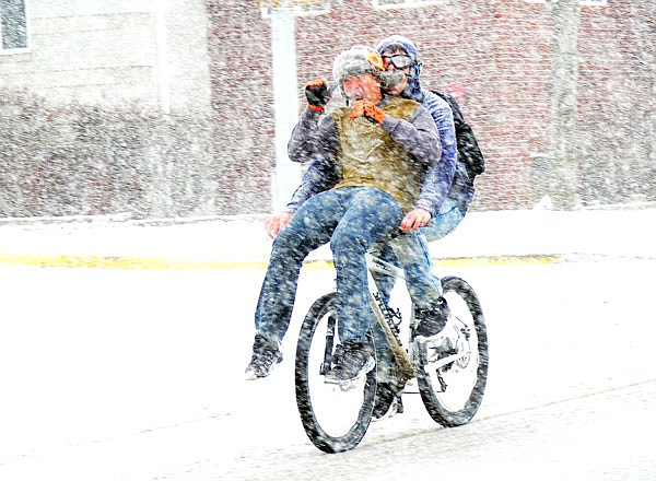 Two students zoom through downtown along McCarty Street on a bicycle as heavy snow falls during the day Friday. A winter weather advisory for Cole County was in effect with 1-3 inches expected.