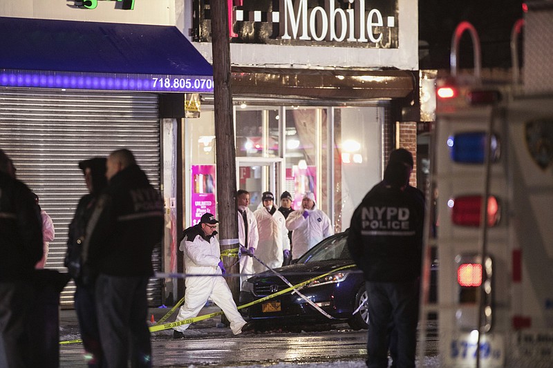 Investigators look over the area after a few New York City police officers were shot while responding to a robbery at a T-Mobile store in the Queens borough of New York on Tuesday, Feb. 12, 2019. An official said one of them was killed. (AP Photo/Kevin Hagen)