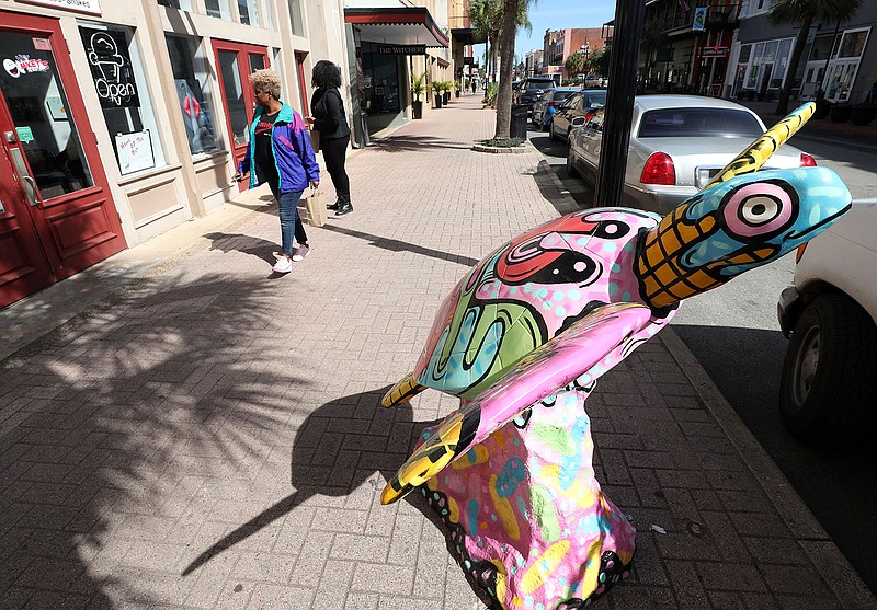 In this Wednesday, Feb. 13, 2019 photo, pedestrians stroll past Hey Mikey's toward one of two sea turtle statues displayed in Galveston, Texas. The Turtle Island Restoration Network is installing statues to promote awareness for sea turtle restoration. (Kelsey Walling/The Galveston County Daily News via AP)