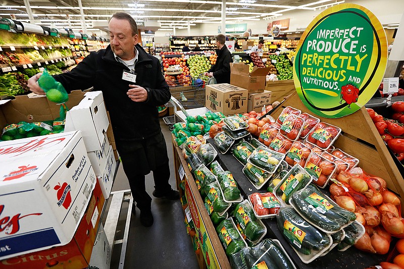 In this Friday, Jan. 18, 2019, photo, assistant produce manager Dave Ruble stocks the imperfect produce section at the Hy-Vee grocery store in Urbandale, Iowa. After enjoying a brief spotlight in supermarket produce sections, blemished fruits and vegetables may already be getting tossed back in the trash. (AP Photo/Charlie Neibergall)