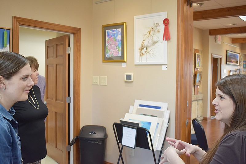 At left, Brandi Rackers chats with Lina Forrester on Sunday about her painting "Stains & Smoke," shown in the background, during Capital Arts Show-Me Art Exhibition, "Art in the Eye of the Beholder." Rackers, of Jefferson City, won the Best of the Show Award in the judged, statewide art exhibit. Forrester is one of the honorable mention winners.