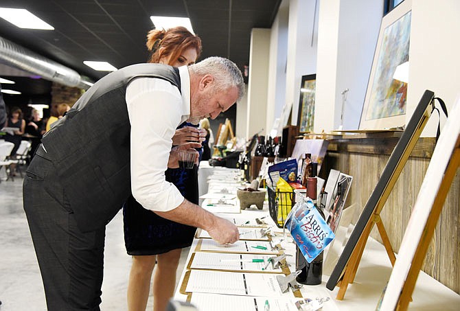 Tim Tinnin bids on items for auction Friday at the 11th annual HALO ArtReach Auction at the Capital Bluffs Event Center. The auction included artwork from local and nationally recognized artists.