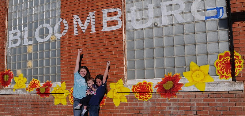 "Yea for us!" Kinsey Mangrum, left, and Ally Dixon, who is holding Britllynn Mangrum, might be saying as they have fun around the newly painted outside wall of the historic Bloomburg State Bank building.