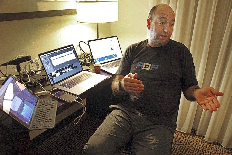 In this Tuesday, March 5, 2019 photo, Art Aldridge of New York City explains how he coordinates live video from checkpoints along the Iditarod Trail Sled Dog Race in remote parts of rural Alaska back to his master control set-up, three laptop computers set up in a darkened hotel room in Anchorage, Alaska. Far from competitors tackling the frozen wilderness in Alaska’s Iditarod Trail Sled Dog Race, a dozen people, including Aldridge, are holed up inside an Anchorage hotel behind banks of computers, tracking the punishing route and connecting with global fans seeking a real-time link to the off-the-grid sport. (AP Photo/Mark Thiessen)