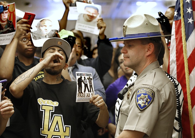 FILE - In this Sept. 2, 2015 file photo, California Highway Patrol Officer J. Nelson stands outside the governor's office as protestors shouting "black lives matter" block the hallway while successfully demanding the passage of AB953, in Sacramento, Calif. California’s first-in-the-nation attempt to track racial profiling complaints against police produced numbers so unrealistically small that the board overseeing the tally wants departments to make changes to encourage more people to come forward. (AP Photo/Rich Pedroncelli, File)