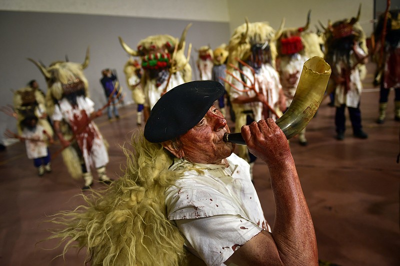 A man plays a horn as "momotxorros " take part in a carnival wearing typical attire, in Alsasua, northern Spain, Tuesday, March 5, 2019. During the carnival "momotxorros" characters, who seem to have been resurrected from a prehistoric ritual, come out onto the streets wearing horns and hiding their faces under headscarves while dressed in a white sheet stained with blood. (AP Photo/Alvaro Barrientos)