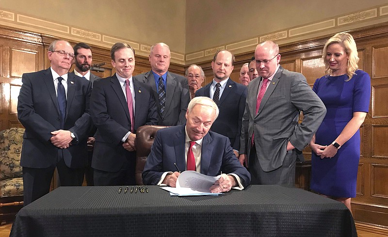 Arkansas Gov. Asa Hutchinson, seated, signs a highway funding bill on Tuesday, March 12, 2019 at the state Capitol in Little Rock, Ark. The legislation raises fuel taxes and taps into expected casino revenue to pay for roads. (AP Photo/Andrew DeMillo)