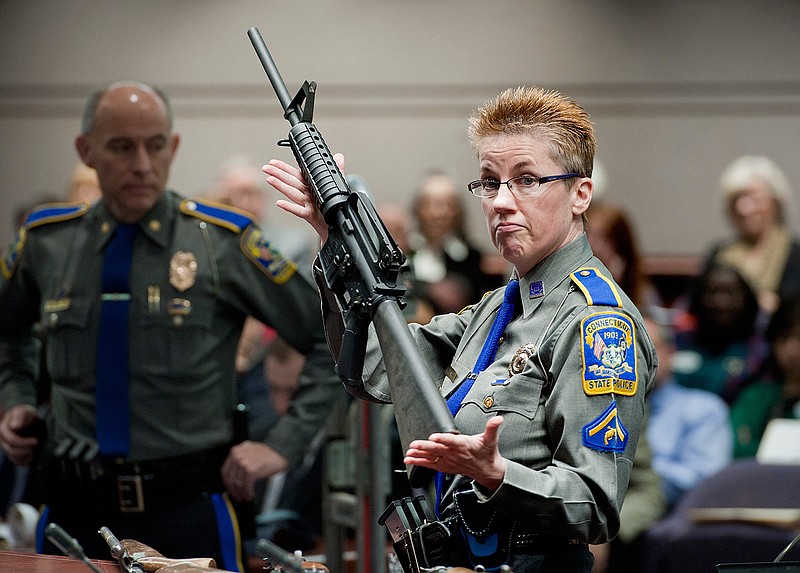 In this Jan. 28, 2013, file photo, firearms training unit Detective Barbara J. Mattson, of the Connecticut State Police, holds a Bushmaster AR-15 rifle, the same make and model used by Adam Lanza in the 2012 Sandy Hook School shooting, during a hearing at the Legislative Office Building in Hartford, Conn. A divided Connecticut Supreme Court ruled, Thursday, March 14, 2019, gun maker Remington can be sued over how it marketed the Bushmaster rifle used in the massacre. (AP Photo/Jessica Hill, File)