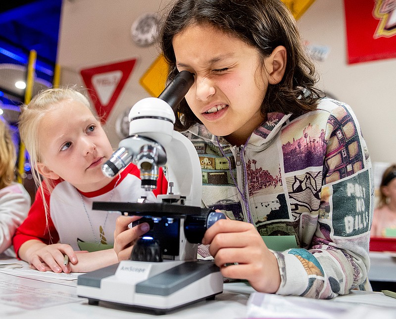 Maggie Pringle, 8, watches as Lia Espinoza, 10, studies a lipstick sample in a microscope during Spy Camp, on Tuesday March 12, 2019, at Longview World of Wonders in Longview, Texas.  One year ago, Spy Camp attracted only 30 young people, but Executive Director Stacey Thompson said interest in solving this year's spring break crime drew a sold-out class of 100 young investigators (Michael Cavazos/The News-Journal via AP)