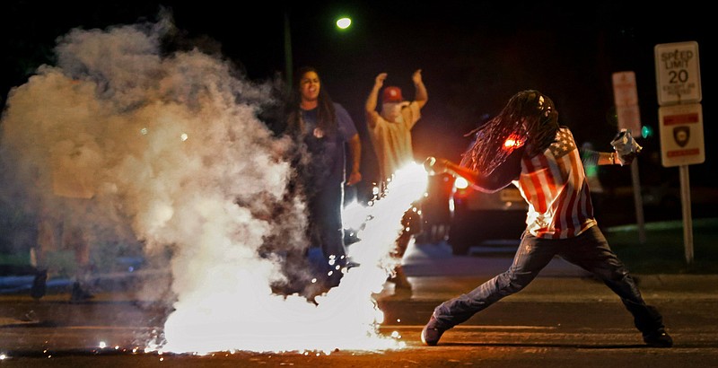 FILE - In this Aug. 13, 2014, file photo Edward Crawford Jr., returns a tear gas canister fired by police who were trying to disperse protesters in Ferguson, Mo. Six young men with connections to the Ferguson protests, including Crawford, have died, drawing attention on social media and speculation in the activist community that something sinister is at play. Police say there is no evidence the deaths have anything to do with the protests and note that only two were homicides. But activists and observers remain puzzled and wonder if they'll ever get answers. Crawford fatally shot himself in May 2017 after telling acquaintances he had been distraught over personal issues, police said. (Robert Cohen/St. Louis Post-Dispatch via AP, File)