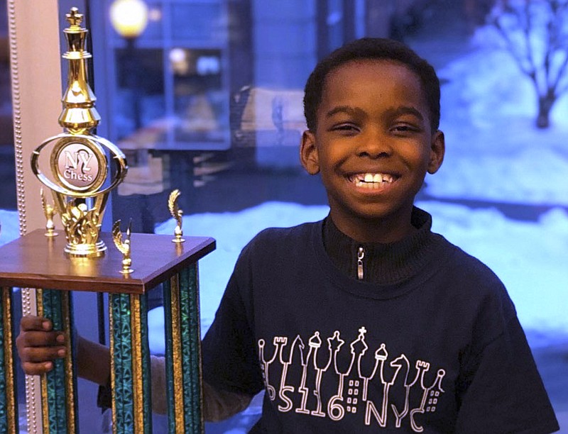 In this photo taken Sunday, March 10, 2019 in Saratoga, N.Y., 8-year-old Tanitoluwa Adewumi poses with his trophy after winning the New York State Scholastic Championships tournament for kindergarten through third grade. The victory will be his family's ticket out of a homeless shelter. Tani and his family have lived in a New York City shelter since fleeing Nigeria in 2017. (Russell Makofsky via AP)