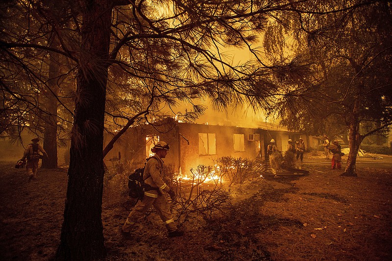 FILE - In this Nov. 9, 2018, file photo firefighters work to keep flames from spreading through the Shadowbrook apartment complex as a wildfire burns through Paradise, Calif. California is calling in the National Guard for the first time to help protect communities from wildfires like the one that destroyed much of the city of Paradise last fall. Starting in April 2019, 110 California National Guard troops will receive 11 days of training in using shovels, rakes and chain saws to thin trees and brush.  (AP Photo/Noah Berger, File)