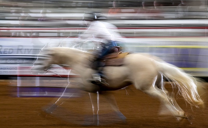 Doreen Rue from Aubrey, Texas, rides her horse, DS Sparkys Leo Kally, towards the finish line of the barrel racing route at the senior world championship barrel race on Thursday at Four States Fairgrounds in Texarkana, Ark. This photo was captured with a method called "panning," where the photographer slows down the shutter speed and moves the camera with the subject as it moves to create a sense of motion within the photograph. As the exposure was being made for this image, another photographer's flash fired and was captured that resulted in the horse and rider being outlined with light.