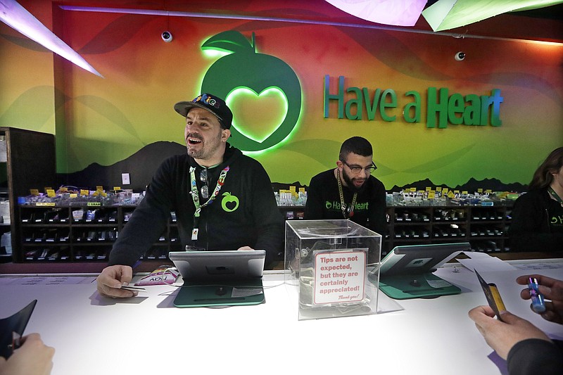 In this photo taken Thursday, March 28, 2019, employees Dan Giroux, left, and Dustin Barrington ring up sales for customers at a marijuana shop in Seattle.  When Washington and Colorado launched their pioneering marijuana industries in the face of U.S. government prohibition, they imposed strict rules in hopes of keeping the U.S. Justice Department at bay. Five years later, federal authorities have stayed away, but the industry says it has been stifled by over-regulation. Lawmakers in both states have heard the complaints and are moving to ease the rules. (AP Photo/Elaine Thompson)