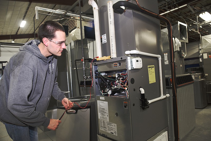 Justin Kleinheider of Washington, Missouri, inspects a furnace to see why the unit does not kick on when the temperature on the thermostat is increased. 