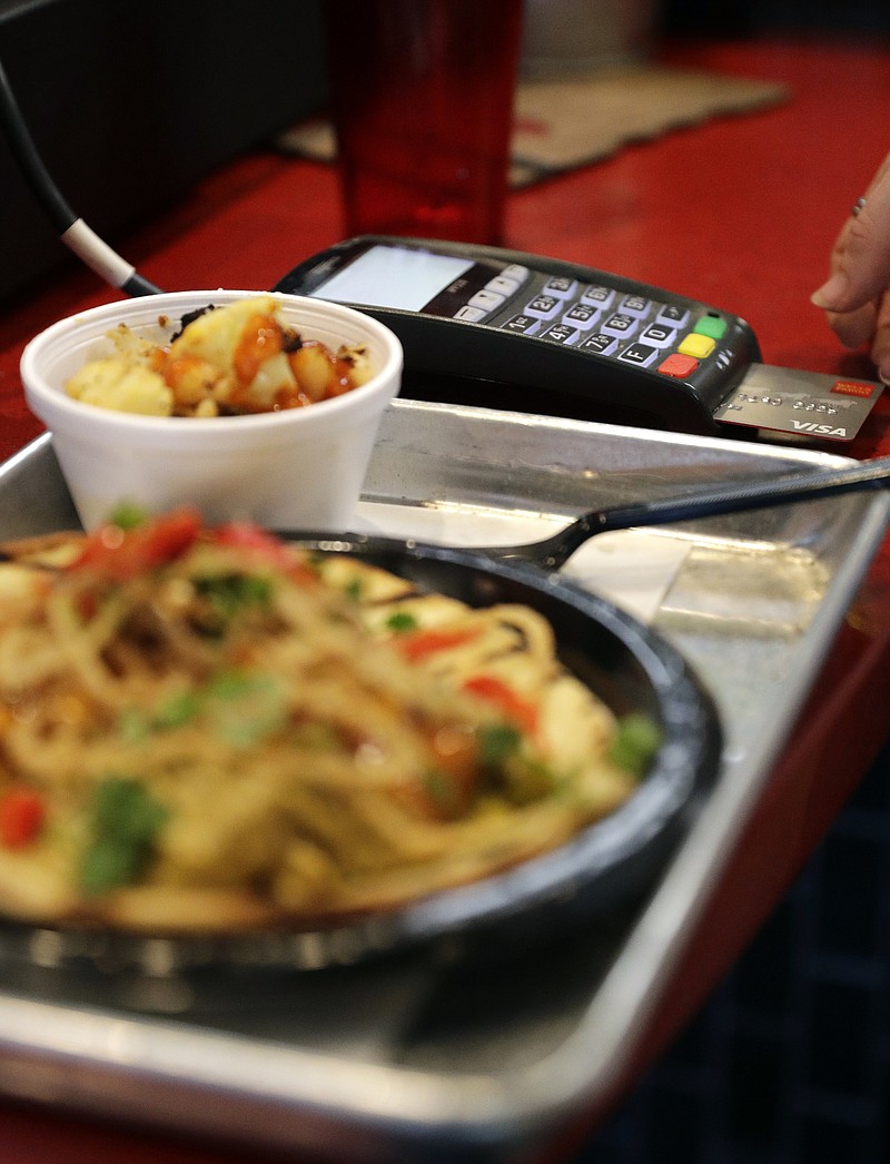 FILE - In this April 10, 2018, file photo, a customers uses a credit card machine to pay for food at Peli Peli Kitchen in Houston. Owner Thomas Nguyen had a change of heart after transitioning one of his three Peli Peli South African fine dining restaurants and his Peli Peli Kitchen fast casual location to a no-cash policy. (AP Photo/David J. Phillip, File)