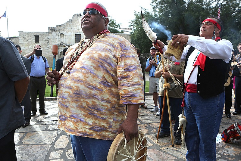 In this July 7, 2015 photo, Epifanio Hernandez, left, and Adrian Ramirez, descendants of Native Americans, give blessing to the four corners of the earth as city leaders celebrate the announcement of the San Antonio's Spanish missions winning World Heritage Site status in front of The Alamo in San Antonio, Two competing requests to designate the Alamo in San Antonio as a Historical Texas Cemetery could change how the mission is remembered. The Texas General Land Office wants to have the Alamo church listed as a historic Texas cemetery, citing the names of three people buried there nearly a century before the 1836 battle. Another proposal from Native American groups seeks a much larger area be designated a cemetery at the revered site. (Bob Owen/The San Antonio Express-News via AP)