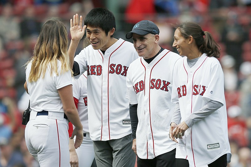 2018 Boston Marathon winners Yuki Kawauchi, left, and Desiree Linden, right, walk off the field with race sponsor John Hancock's Rob Freidman, center, after throwing out the ceremonial first pitch before a baseball game between the Boston Red Sox and the Baltimore Orioles in Boston, Saturday, April 13, 2019. (AP Photo/Michael Dwyer)
