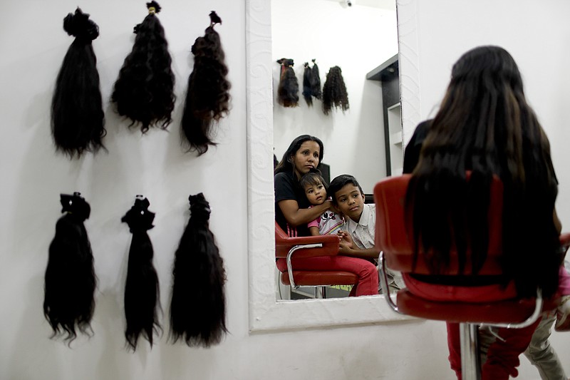 Nelly Navarro sits with her kids Nerianny and Luis in a beauty salon where she came to consult how much money she could get for her hair, in Caracas, Venezuela, Tuesday, April 2, 2019. Navarro said she needs the $100 to travel to Colombia where she's planning to move. (AP Photo/Natacha Pisarenko)