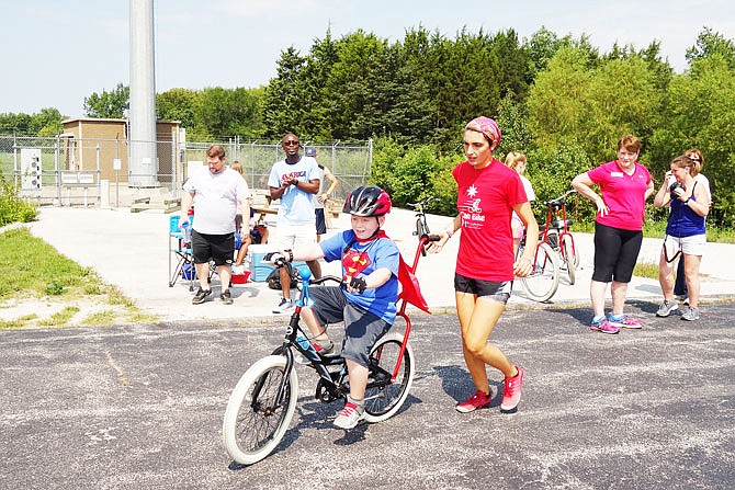 iCan Bike Camp volunteers and parents cheer as Matthew Hoover, 8, makes his first laps of the outdoor course in 2017. iCan Shine employee Amy Casale helps him steer and stay steady. This year's camp is June 17-21.
