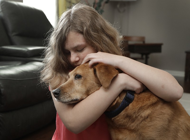 Sobie Cummings, 11, plays with her dog, Dallas, at the family's home in Waxhaw, N.C., Friday, March 29, 2019. A psychiatrist suggested that a service dog might help to ease Sobie’s crippling anxiety and feelings of isolation. But when they brought home a $14,500 Briard from Mark Mathis’ Ry-Con Service Dogs, Okami broke from Glenn Cummings' grasp and began mauling Dallas. (AP Photo/Chuck Burton)