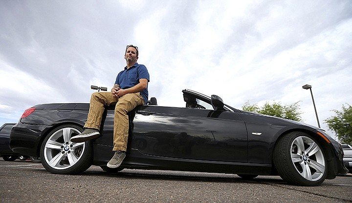 In this April 23, 2019, photo, Chris Williamson poses for a photo sitting on his car in Phoenix. When Williamson was in the market for a new family car, a timely ad and conversations with a co-worker convinced him to try something out of the ordinary. He bought the BMW 3 Series convertible and covers the payments by renting it to strangers on a peer-to-peer car sharing app called Turo. It allows his family of seven to have a nicer car, essentially for free. (AP Photo/Ross D. Franklin)