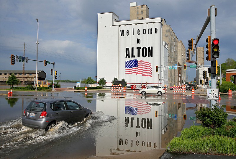 A vehicle drives through Mississippi River flood water in downtown Alton, Il. on Monday, May 6, 2019. Flooding from the Mississippi River closed streets in downtown, forced the closure of Argosy Casino and flooded the basements of several businesses. The Mississippi River is expected to crest at 34.8 feet later on Monday, almost 14 feet above flood stage. The red painted line beneath the American flag on the grain silos denotes the height of flood water in 1993. (David Carson/St. Louis Post-Dispatch via AP)