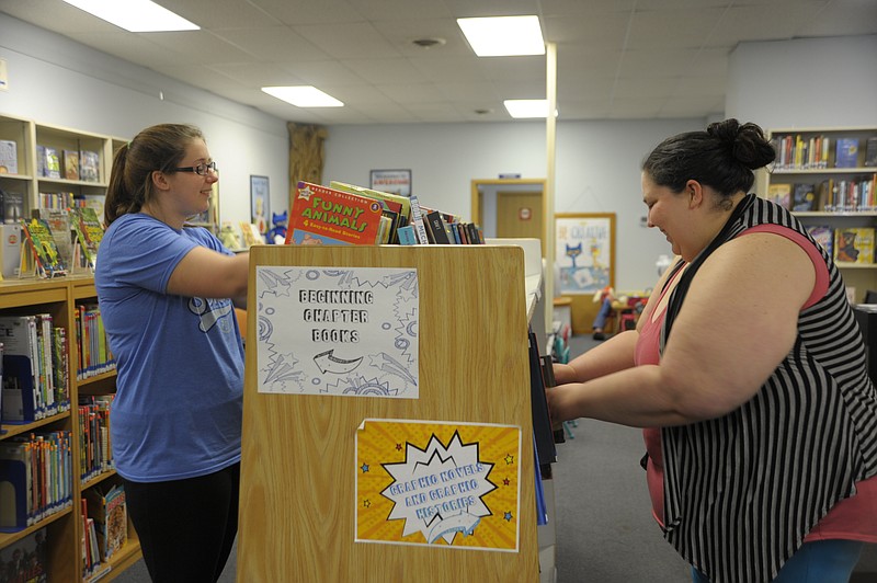 Library assistants Taylor Ireland and Heidi Porter stock the youth shelves at the Moniteau County Library. Kindergarten through eighth-graders are eligible to participate in 'A Universe of Stories' summer reading program.