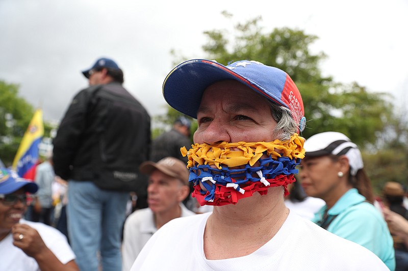 An opponent of the Nicolas Maduro government, his mouth covered with strands representing the national colors of Venezuela, waits for the arrival of opposition leader Juan Guaidó to lead a rally in Caracas, Venezuela, Saturday, May 11, 2019. Guaidó has called for nationwide marches protesting the Maduro government, demanding new elections and the release of jailed opposition lawmakers. (AP Photo/Martin Mejia)