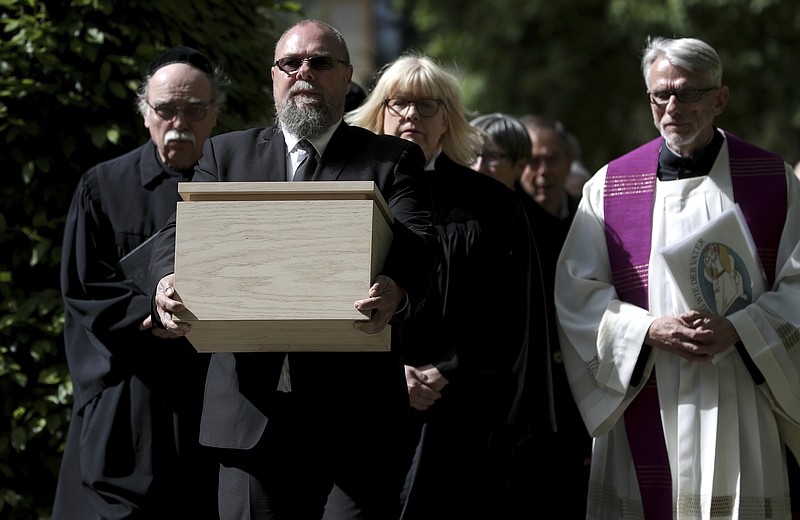 A cemetery staff member holds a box with the remains of political prisoners of the Nazi regime in Berlin, Germany, Monday, May 13, 2019. Some 300 microscopic tissue samples belonging to resistance fighters, mostly women, who were executed during the Third Reich at Berlin's Ploetzensee prison were buried during a ceremony at the Dorotheen cemetery in Berlin on Monday. (AP Photo/Michael Sohn)