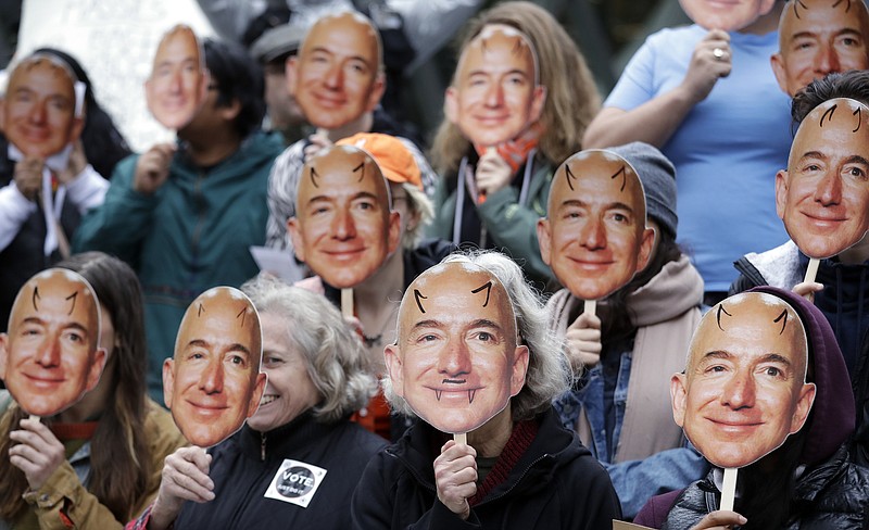 FILE - In this Oct. 31, 2018, file photo, demonstrators hold images of Amazon CEO Jeff Bezos near their faces during a Halloween-themed protest at Amazon headquarters over the company's facial recognition system, "Rekognition," in Seattle. San Francisco is on track to become the first U.S. city to ban the use of facial recognition by police and other city agencies as the technology creeps increasingly into daily life. Studies have shown error rates in facial-analysis systems built by Amazon, IBM and Microsoft were far higher for darker-skinned women than lighter-skinned men. (AP Photo/Elaine Thompson, File)