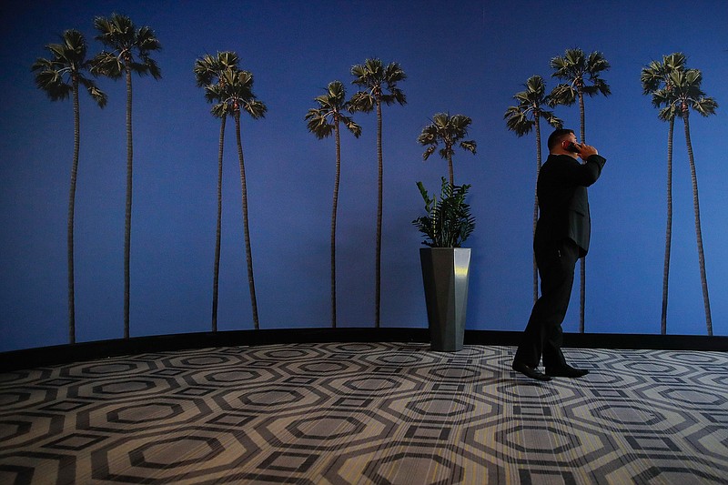 In this May 4, 2018, file photo a man talks on the phone in a hallway adorned with the palm tree-printed wallpaper at a hotel near the Los Angeles International Airport in Los Angeles. U.S. regulators are proposing new measures intended to thwart billions of annoying robocalls received by Americans each year. The rising volume of unwanted calls in the last few years has created pressure on Congress, regulators and phone companies to do something to act. (AP Photo/Jae C. Hong, File)