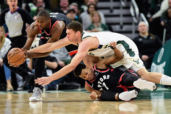 Brook Lopez of the Bucks battles Raptors teammates Kyle Lowry (7) and Serge Ibaka (9) for the ball and picks up a foul on the play during Friday night's game in Milwaukee.