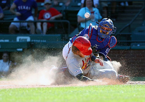 Harrison Bader of the Cardinals  slides safely home as the ball deflects off of his back away from Rangers catcher Jeff Mathis in the 10th inning of Sunday afternoon's game in Arlington, Texas.