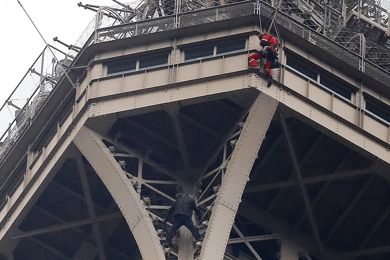A rescue worker, top in red, hangs from the Eiffel Tower while a climber is seen below him between two iron columns Monday, May 20, 2019 in Paris. The Eiffel Tower has been closed to visitors after a person has tried to scale it. (AP Photo/Michel Euler)